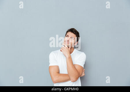 Pensive attractive young man smiling and thinking over grey background Stock Photo