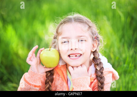 Sweet girl with a fallen toth holding an apple in her hand on nature Stock Photo