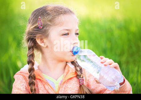 Little cute girl on the nature drinks water from a plastic bottle Stock Photo
