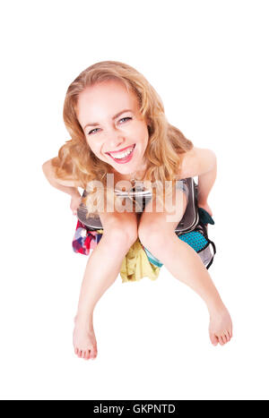 Pretty funny woman sitting on a suitcase with clothing in the studio Stock Photo