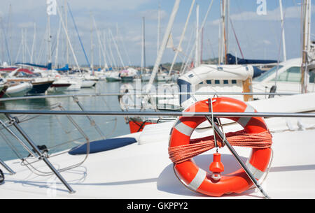 Red life buoy detail on boat in dock of harbor pier with many sailing boats out of focus in background Stock Photo