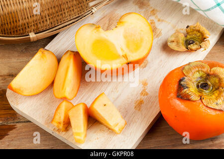 Persimmon yellow color ripe split fruits on wood table Stock Photo