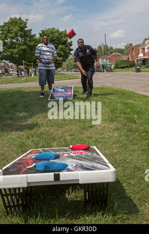 Detroit, Michigan - Neighborhood groups hold a summer street fair. A policeman joins community members in playing cornhole. Stock Photo