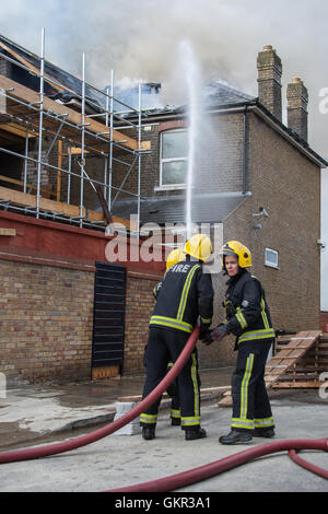 London firefighters at the scene of a hotel fire in East London as flames break through the roof of the property. Stock Photo