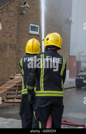 Two London firefighters using a hose whilst operating a height platform at the scene of a fire in London Stock Photo