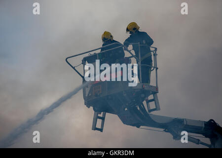 Two London firefighters and smoke whilst operating a height platform at the scene of a fire in London Stock Photo