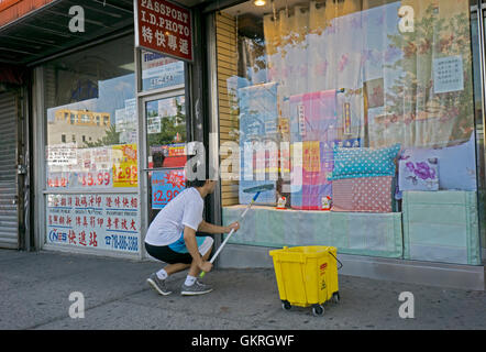 A young Asian man cleaning windows of a bedding store on Main Street in Chinatown, Flushing, Queens, New York Stock Photo