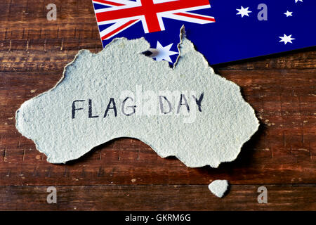 closeup of an Australian flag and a piece of paper cut in the shape of Australia with the text flag day handwritten in it Stock Photo