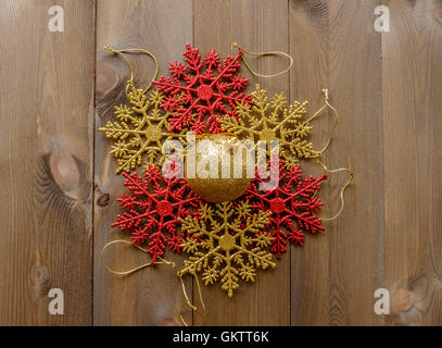 Group of sparkly Christmas tree decorations lay flat on wooden background. Red and gold glitter snowflakes in circle with one go Stock Photo