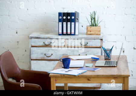 Home office interior in loft space with white brick walls. Cozy workplace with wooden table, office supplies, documents Stock Photo
