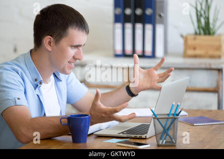 Young stressed businessman sitting with laptop gesticulating with angry and furious expression. Annoyed business man looking Stock Photo