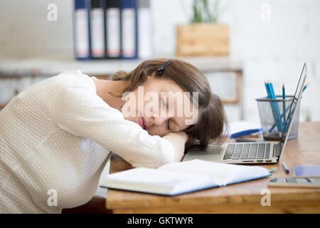 Portrait of young woman lying on the table in front of laptop, sleepy, tired, overworked or lazy to work. Attractive business Stock Photo