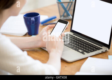 Close-up rear view of young business woman working in office interior on pc, holding smartphone, looking at screen Stock Photo