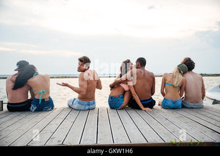 Sad confused young man sitting between happy hugging couples on pier Stock Photo