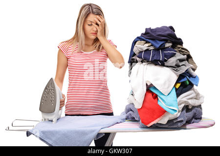 Sad woman posing next to a big pile of clothes and an ironing board isolated on white background Stock Photo