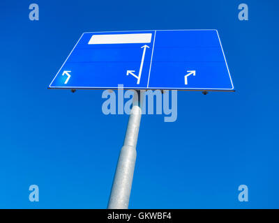 Blank blue direction sign pointing in different directions against blue sky Stock Photo