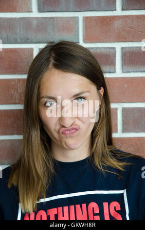 Beautiful young woman making funny faces on a brick wall background Stock Photo