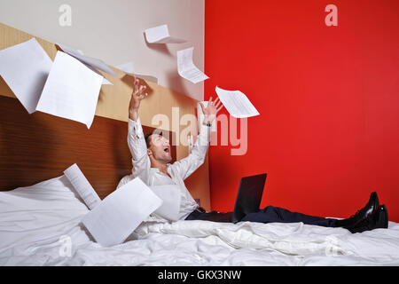 To hell with the job. Businesswoman throws documents. Man with laptop sitting on the couch, and fly papers around him. Deadline. Stock Photo