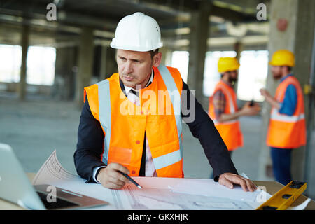 Serious constructor looking at data in laptop display while drawing sketch Stock Photo