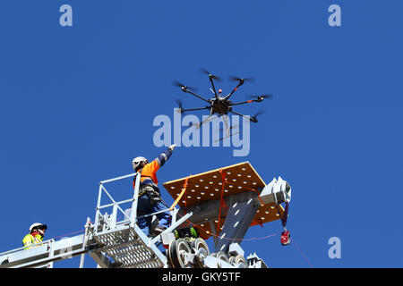El Alto, Bolivia, 23rd August 2016. A technician reaches for a drone as it lands on top of a cable car pylon. The drone is being used to carry a light synthetic cable of a new cable car / gondola lift currently under construction between Rio Seco and La Ceja in El Alto. This is the first part of the process to install the final steel cable that will carry the gondolas. This cable car is one of a second phase of cable car lines that are part of an ambitious project to relieve traffic congestion. 3 routes from the first phase are already operating between the cities of La Paz and El Alto. Stock Photo