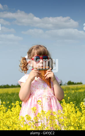 little girl standing in yellow flower field and play pan pipe Stock Photo