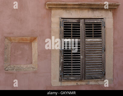 pink wall with stone frame of blocked up cavity alongside old shuttered window with faded paint in walled Old Town Dubrovnik Stock Photo