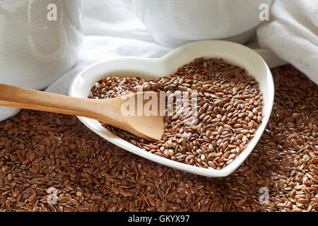 Flax seeds in heart shaped ceramic bowl with wooden spoon Stock Photo