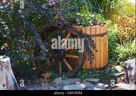 wooden wheel and barrel in the garden as decorative elements Stock Photo