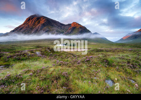 Stunning sunrise over a cottage beneath the mountains at Glencoe in the Scottish Highlands