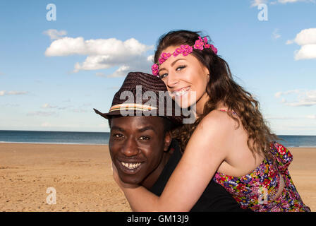 Multicultural mixed race  young couple at beach piggybacking laughing  happy having fun head and shoulders Stock Photo