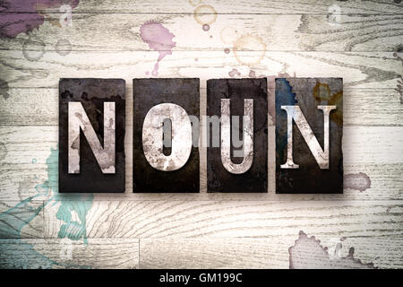 The word 'NOUN' written in vintage dirty metal letterpress type on a whitewashed wooden background with ink and paint stains. Stock Photo