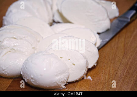 Sliced fresh mozzarella cheese on wooden cutting board and a knife Stock Photo