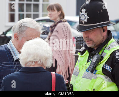 Police officer in traditional helmet  in conversation with two seniors Stock Photo