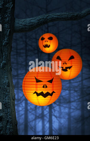 Halloween paper lanterns hanging on a branch in a spooky and foggy forest at night. Stock Photo