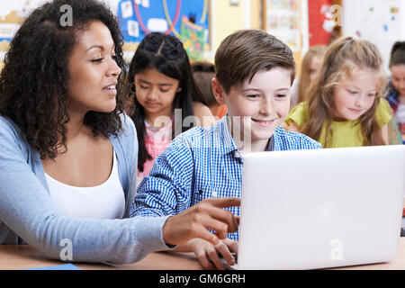 Teacher Helping Male Elementary Pupil In Computer Class Stock Photo - Alamy