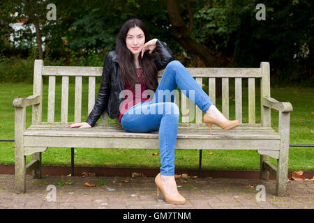 young woman sitting on a park bench posing Stock Photo