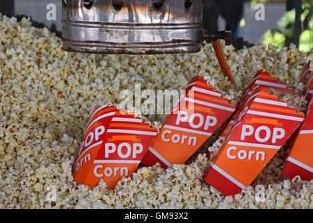 Pile of fresh popcorn and portions in bags made by antique hot air popper machine. Salty snack. Stock Photo