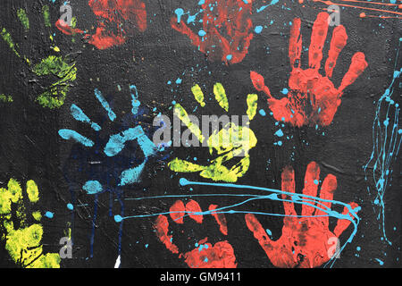 Messy handprints and dripping paint on textured wall background. Colorful hand imprints abstract pattern. Stock Photo