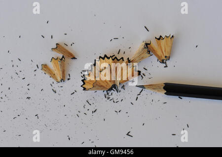 Sharpened graphite pencil and shavings on white paper. Abstract background. Stock Photo