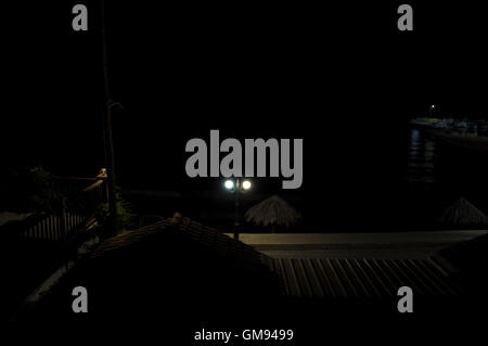 Seaside village on quiet summer night. Dark sea and pier with fishing boats illuminated by street lights. Stock Photo