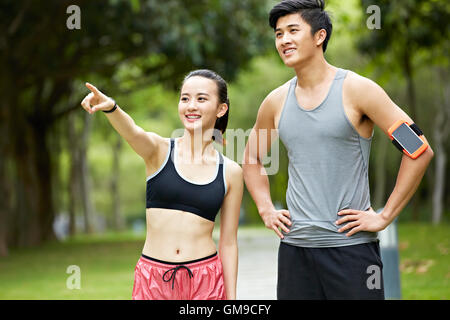 young asian couple exercising in park, woman pointing at something in the distance. Stock Photo