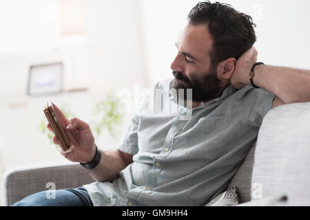 Mid-adult man using smartphone on couch Stock Photo