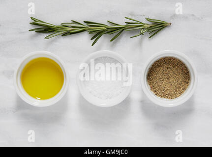 Overhead view of bowl of olive, salt, pepper and rosemary on marble table Stock Photo