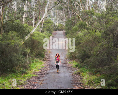 Australia, New South Wales, Katoomba, Young woman walking along empty road in forest Stock Photo