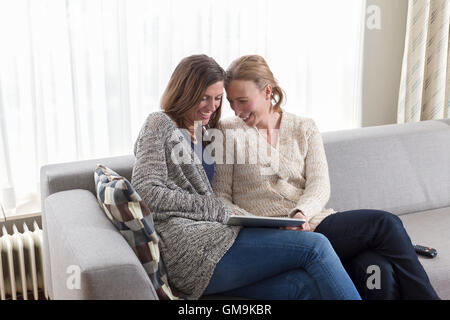 Women sitting on sofa and laughing looking at tablet Stock Photo