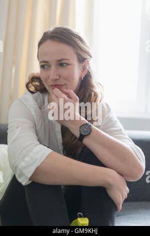 Mid-adult woman sitting on sofa with legs curled up