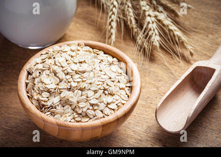 Rolled oats (oat flakes), milk and golden wheat ears on wooden background. Raw food ingredients, healthy lifestyle, cooking food Stock Photo
