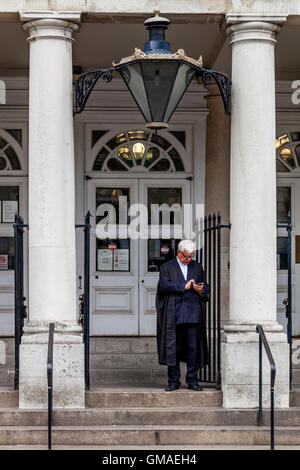 A Lawyer Stands On The Steps Of Lewes Crown Court Texting, Lewes, East Sussex, UK Stock Photo