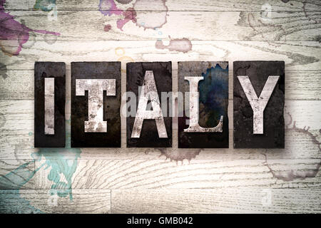 The word 'ITALY' written in vintage dirty metal letterpress type on a whitewashed wooden background with ink and paint stains. Stock Photo