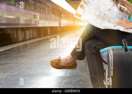 woman with map sitting on chair beside railway in train station Stock Photo